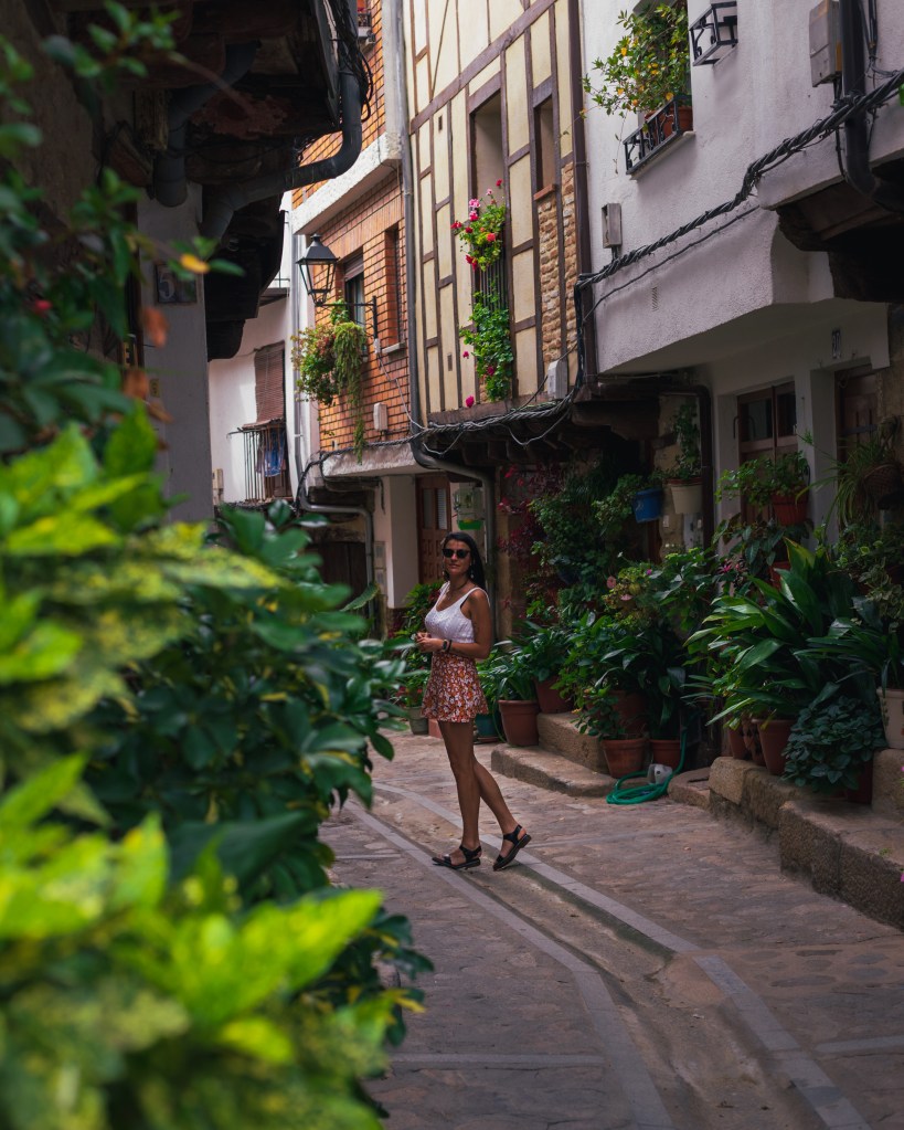Una chica posando en la calle de un pueblo rodeada de plantas