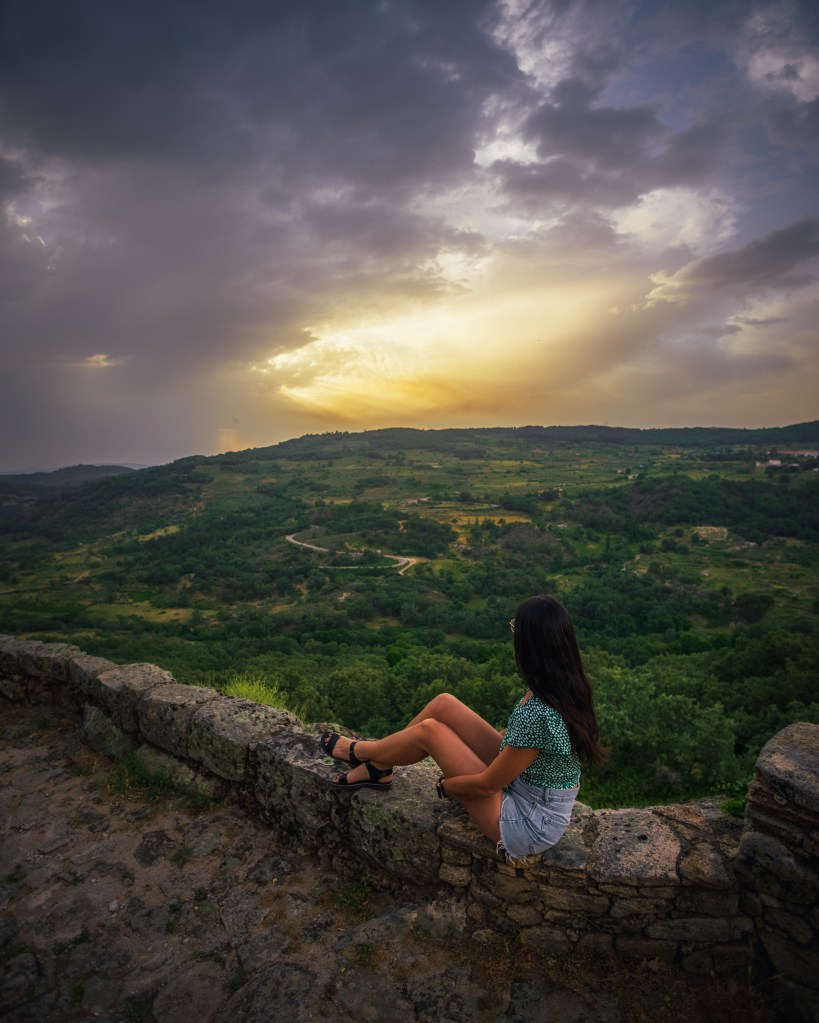 Una chica sentada en lo alto de un muro mirando el atardecer